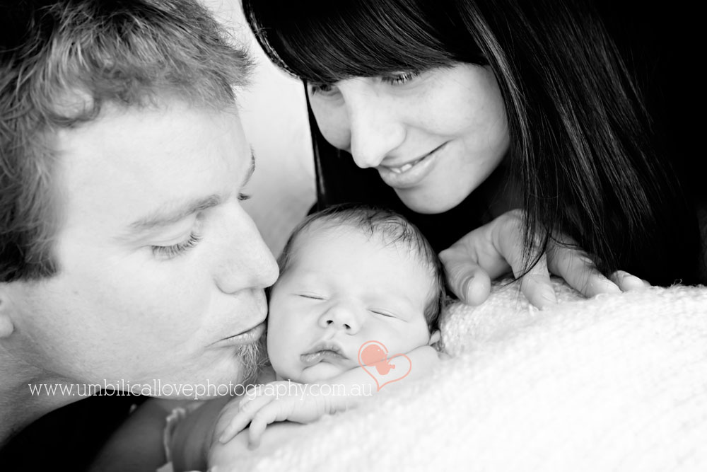 dad kissing newborn with mum looking on smiling