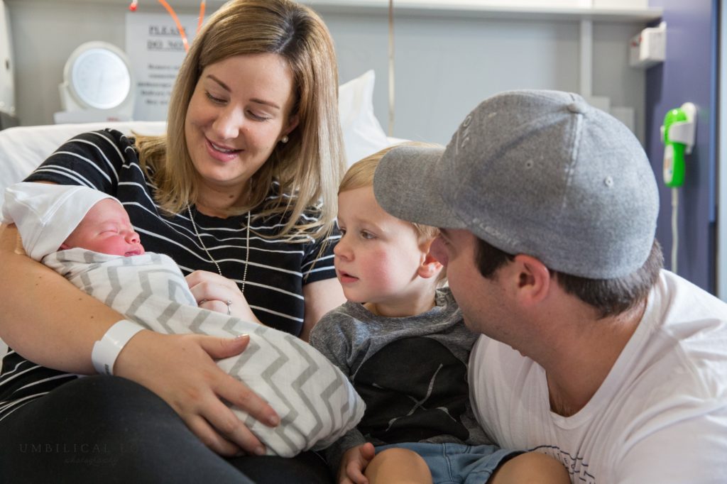 mum, dad and toddler look at new baby brother