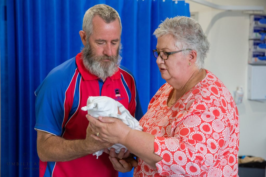 grandparents hold newborn son together 
