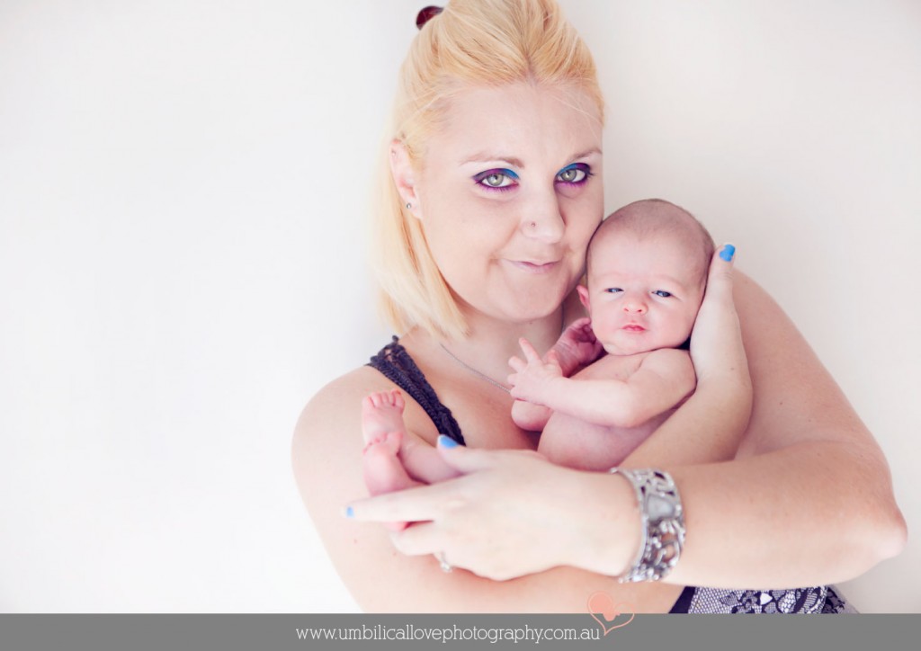 mum holding her new baby tight in her arms and looking at the camera