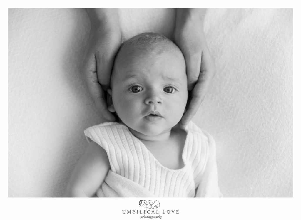 baby boy lying on blanket with mums hands around head