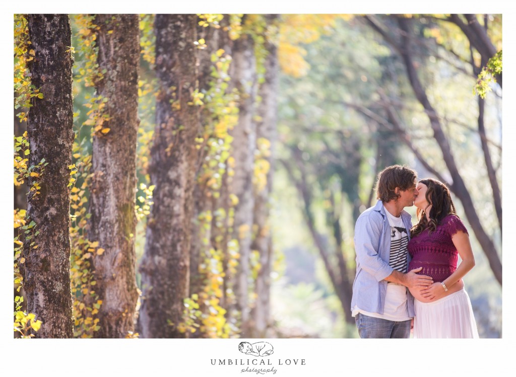 Couple kisses as they hold her pregnant tummy