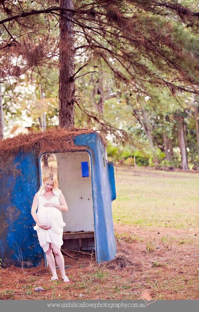 pregnant lady looking down holding her belly under a pine tree
