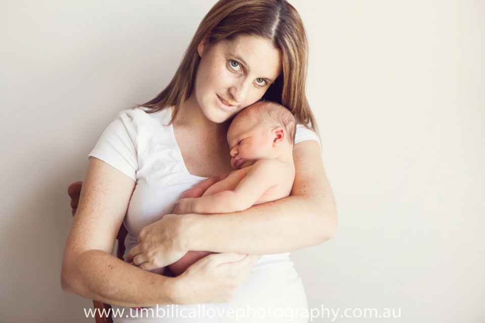 mother cradling newborn in her arms and smiling at the camera