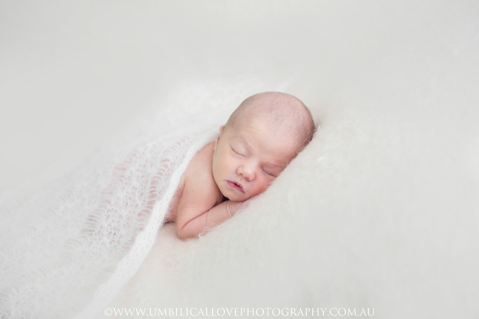 Newborn-Baby-Photography-Wagga-Wagga baby lying on a soft white blanket covered with thin knittes wrap