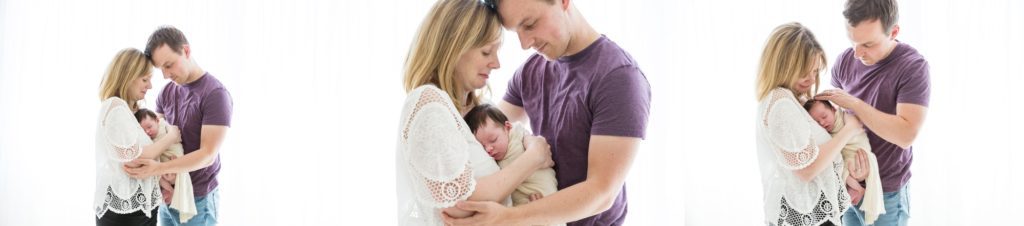 Mum and dad cuddle their newborn baby girl as she sleeps in their arms