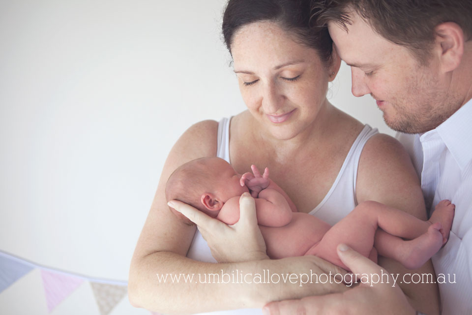 mum holding her new baby close and dad in close admiring the new family addition 