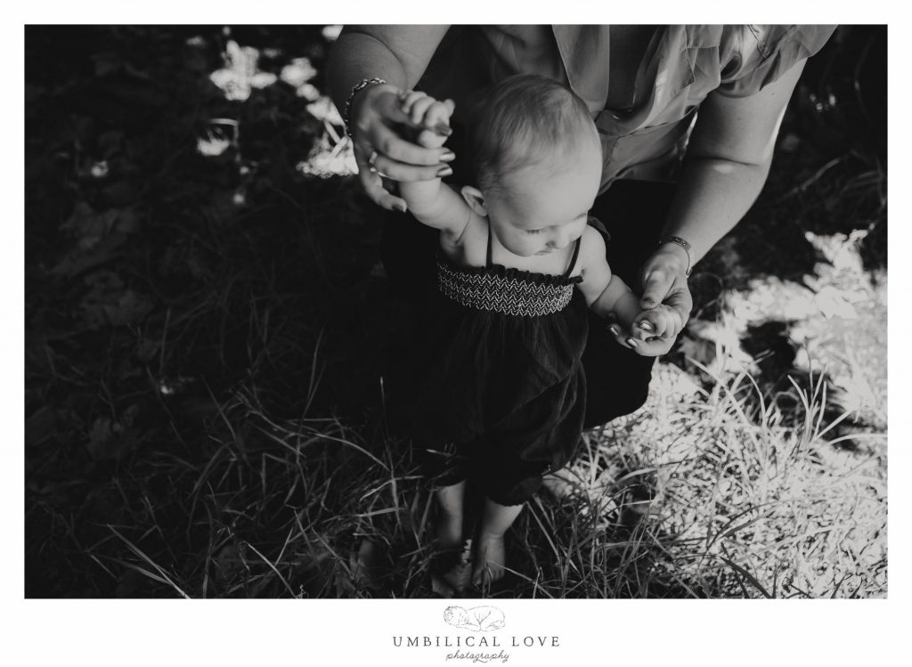 mum holds little girls hand while she takes her first steps 