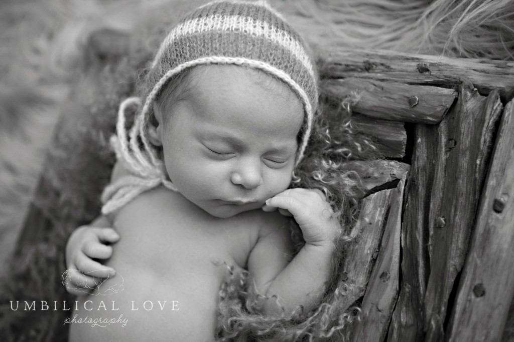 black and white of newborn sleeping on his back with her face resting on her hand
