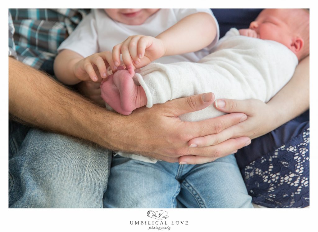 Big brother tickling toes of newborn baby sister