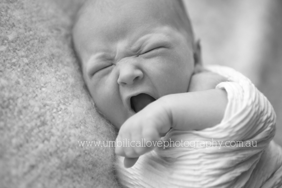 newborn baby wrapped up and having a big yawn