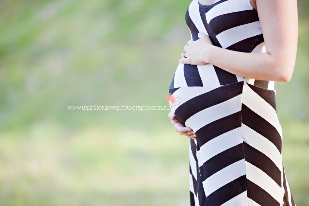 32 weeks gestation pregnant lady holding her belly standing in a field on the side