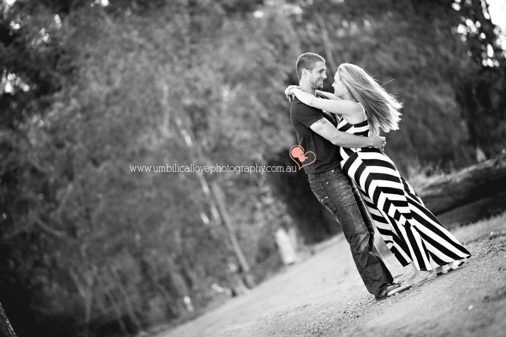 pregnant lady arms around husbands neck hair blowing in the breeze