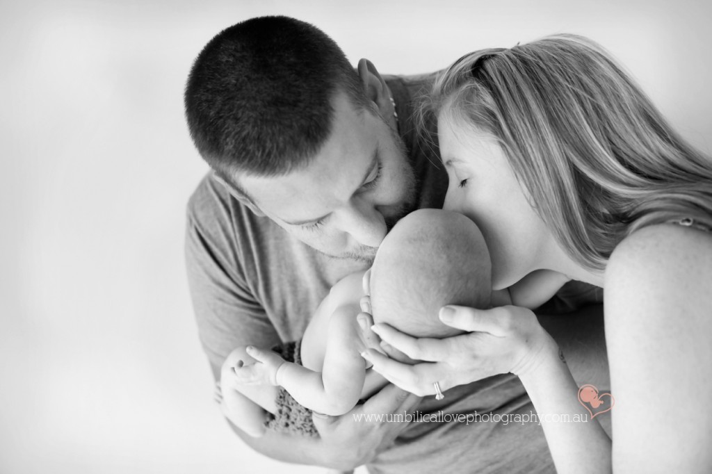 mum & dad holding their 6 week old son leaning over giving him a tender kiss