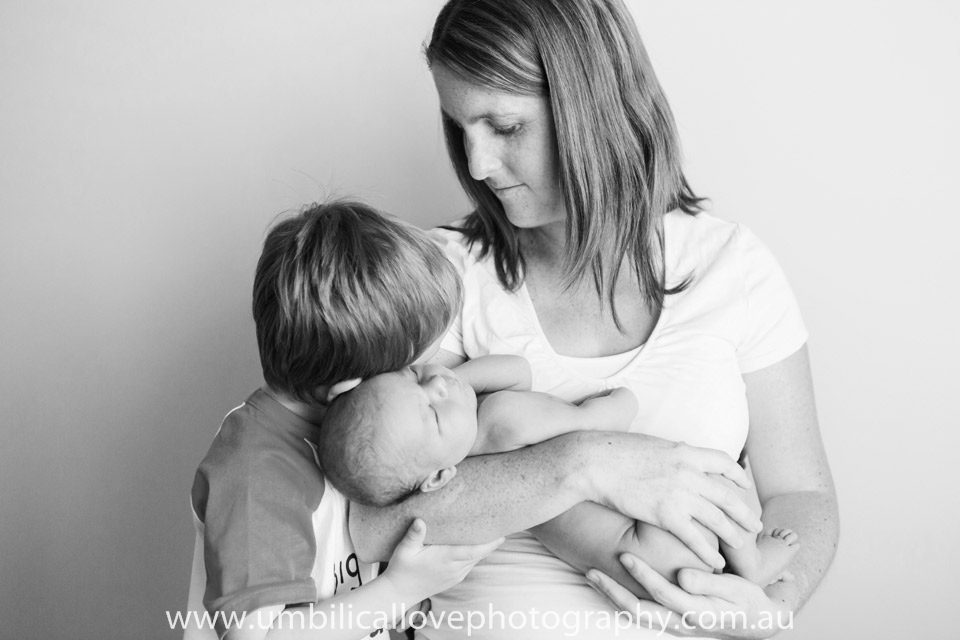 mother and sibling hugging newborn