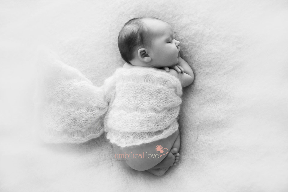 baby curled up on a white throw