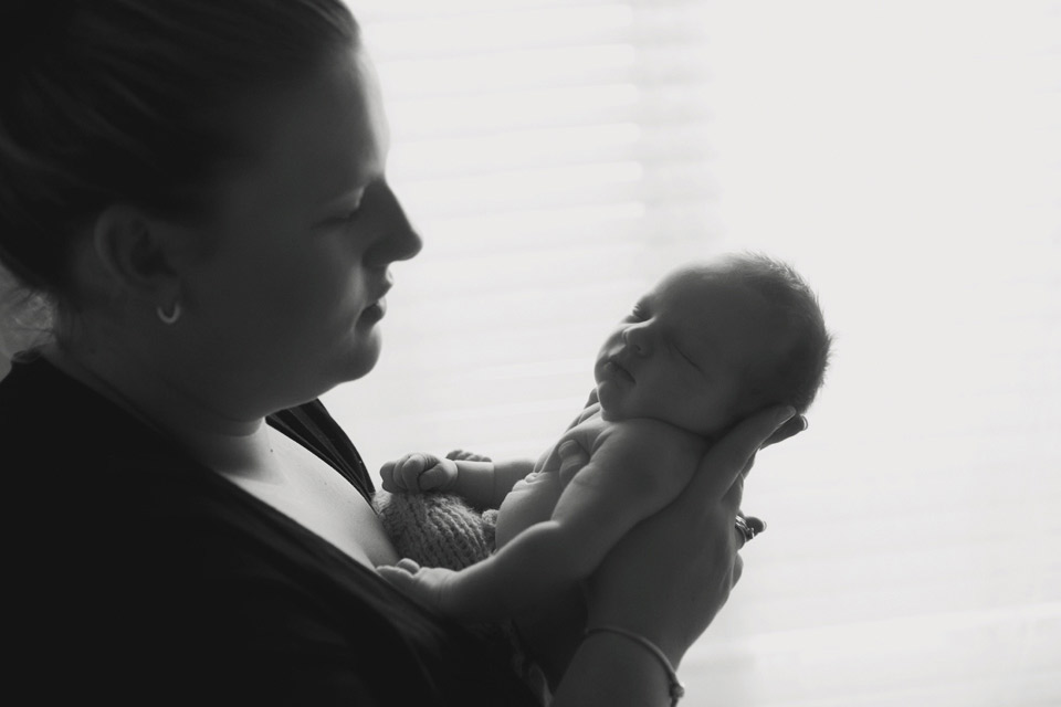 intimate image of a new mum holding her newborn baby looking lovingly into his face near a window