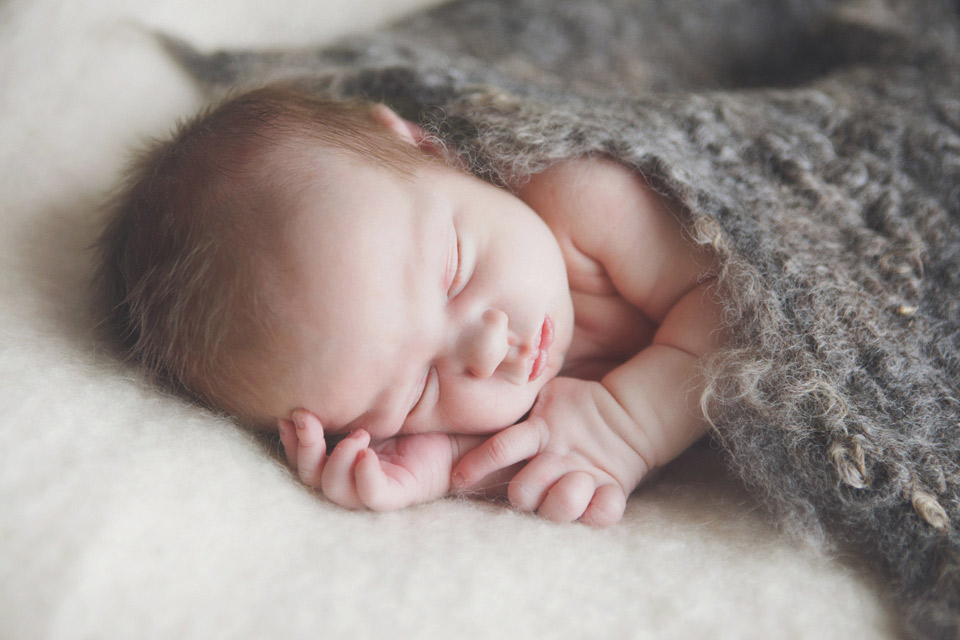 image of a new baby sleeping on textured blanket with a felt wrap on top