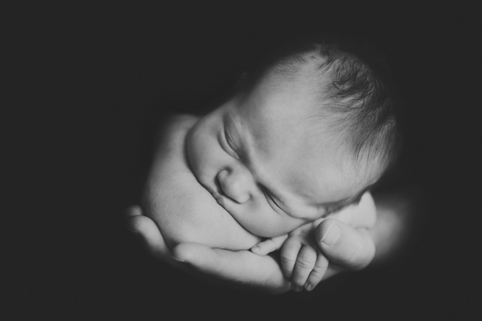 beautiful black and white image of just dads hand holding his new baby's face and arms looking at the camera