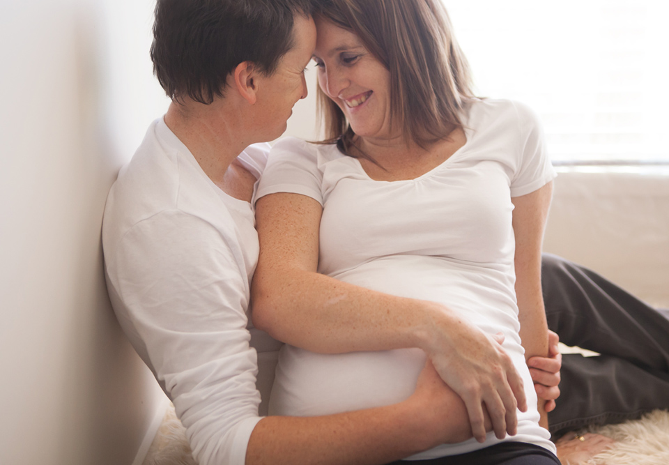 couple sitting down looking at each other laughing cuddling the lady's pregnant belly