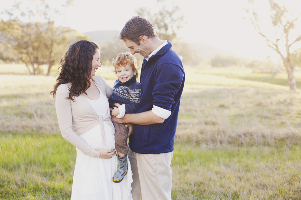 mum and dad holding & hugging their toddler and holding their pregnant belly
