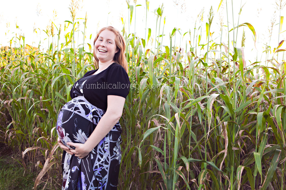 pregnant lady holding underneath her belly laughing at the camera