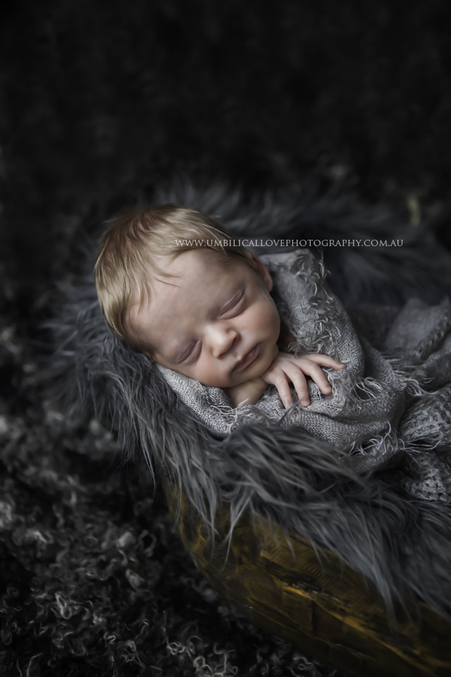 newborn baby boy 7 days old swaddled sleeping on his arm on top of a fleecy fur