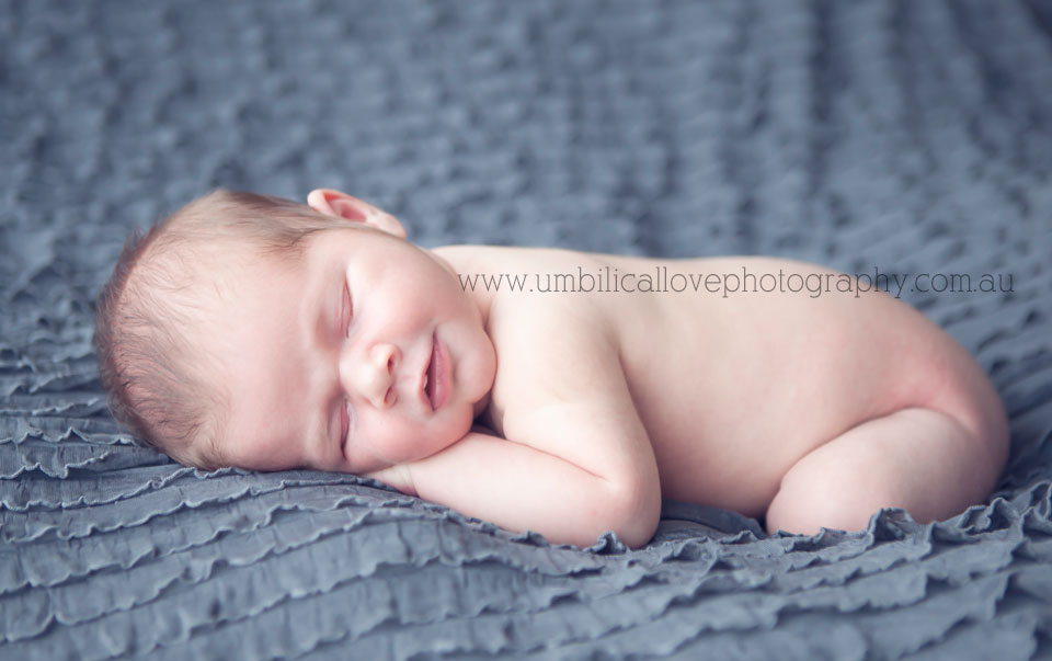 beautiful newborn baby boy laying on a layered blanket with a wind smile