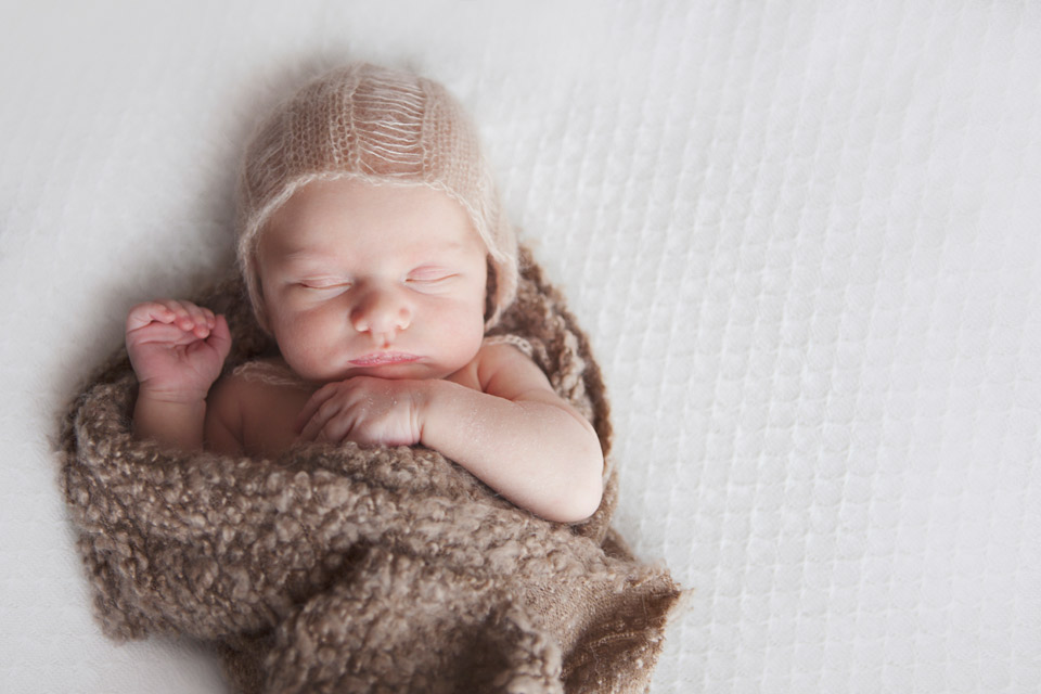 baby asleep with a little knitted hat on and wrapped in a textured material