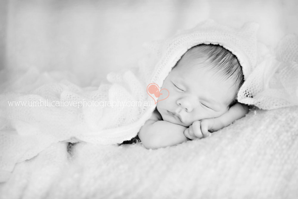 baby laying on arms asleep with blanket draped over her head