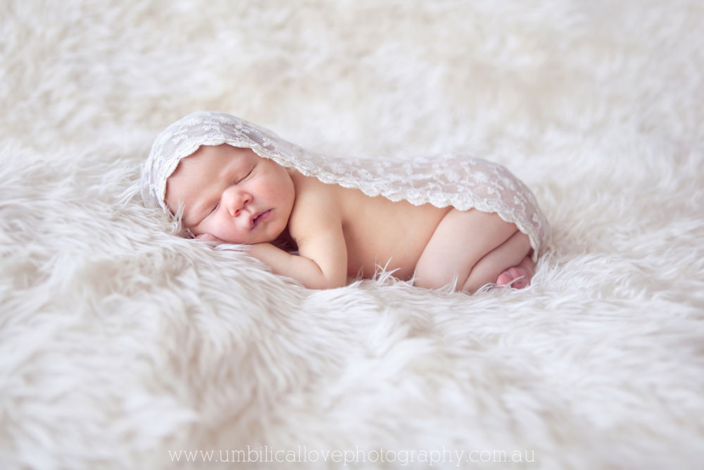 gorgeous newborn baby girl laying in sheeps fleece on her arms