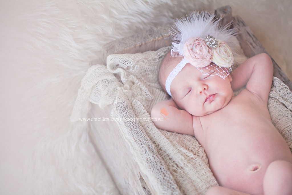 baby with fascinator on her head sleeping with her ams behind her head relaxing 