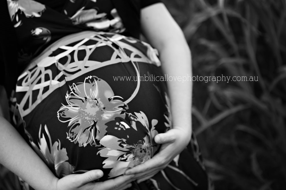 lady sitting in the grass holding her pregnant belly