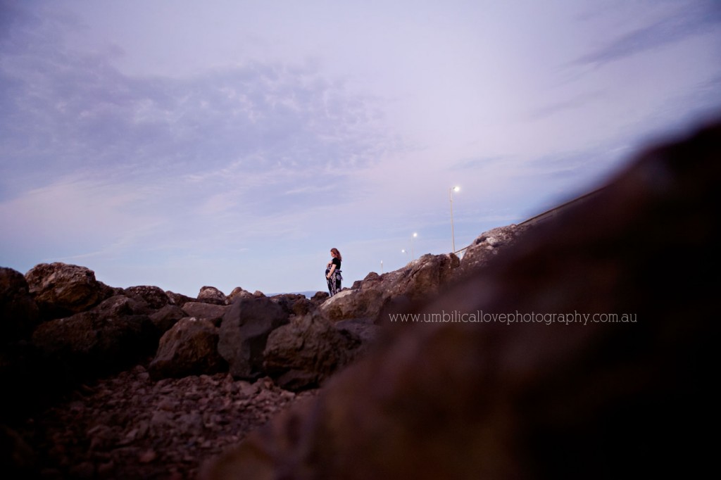 looking out to see holding pregnant belly with rocks in the foreground