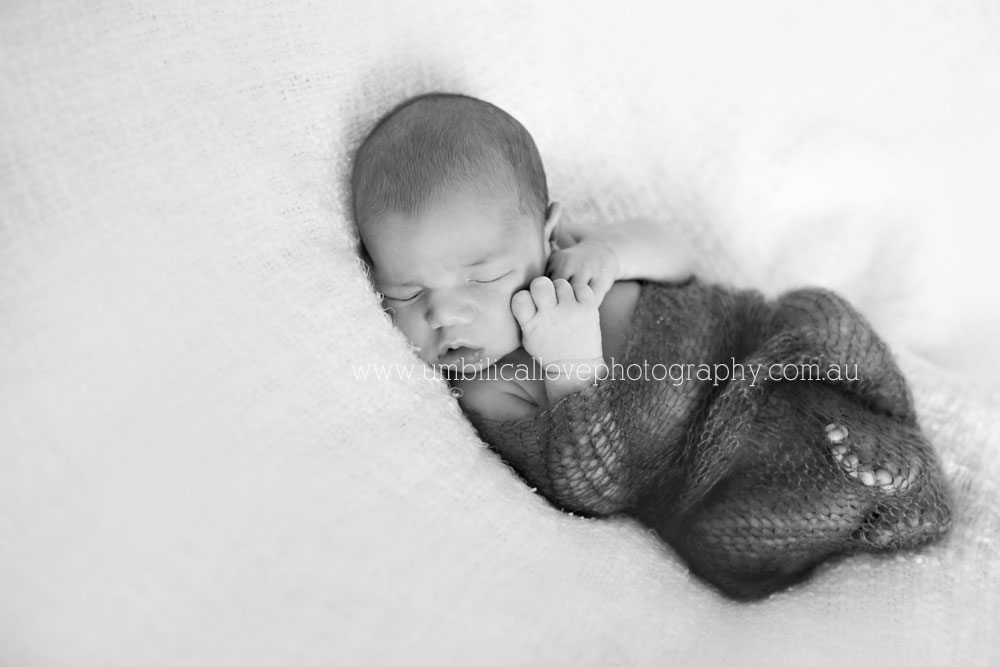 newborn wrapped up lying on his back with hands to face