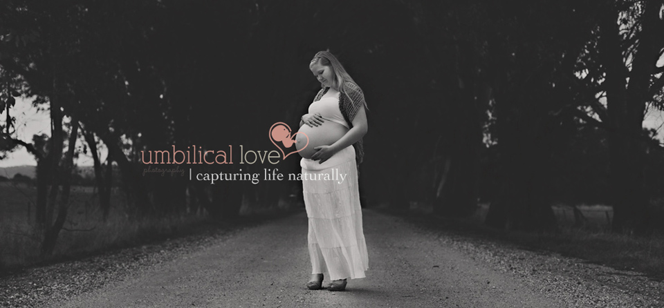pregnant woman standing on a dirt rd looking down with her hands on her bare belly
