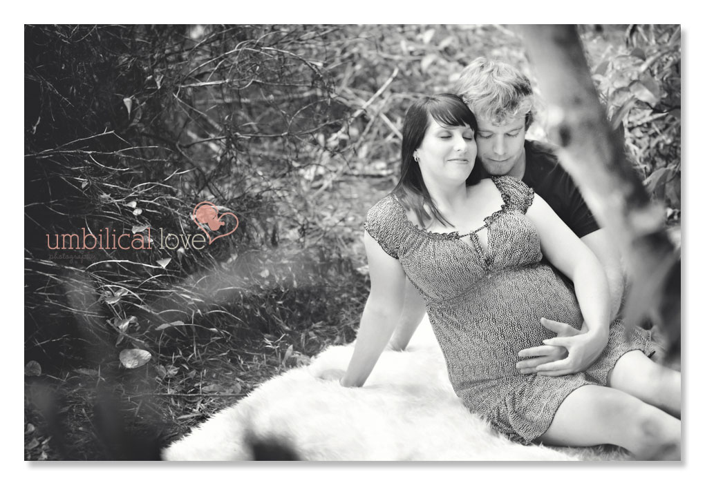 husband cuddling his wifes pregnant belly in the bush eyes closed