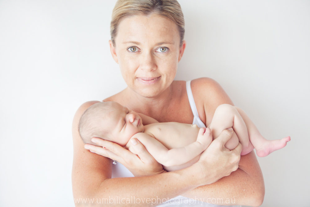 gorgeous new mum cradling her newborn sleeping daughter looking at the camera