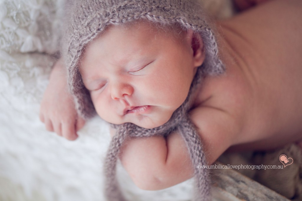beautiful newborn baby sleeping with wrinkles in her back with a fine knitted bonnet on