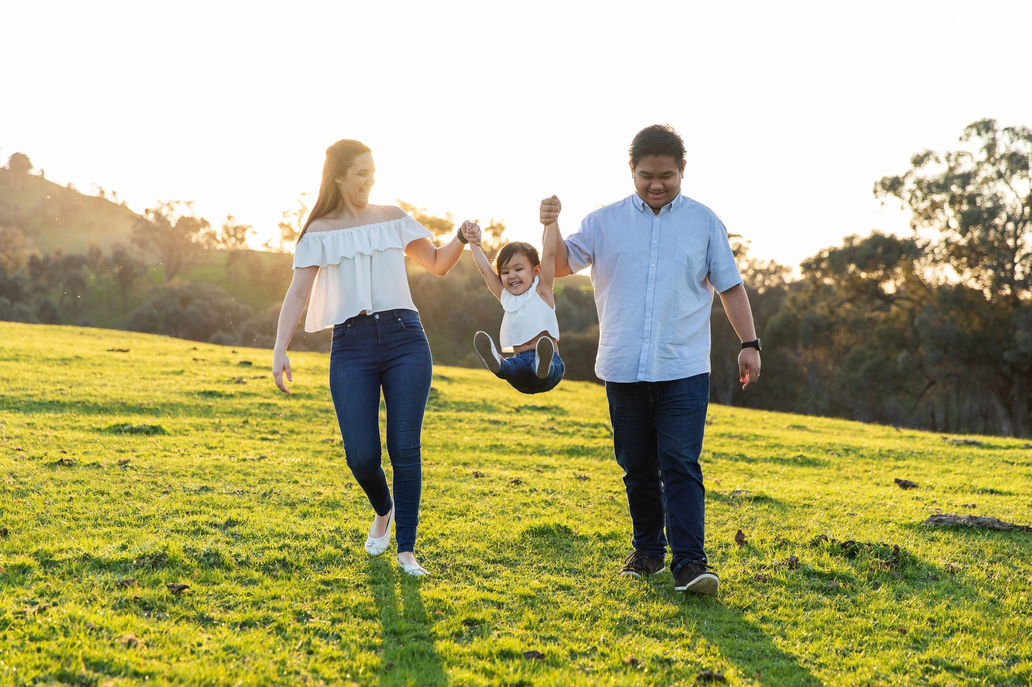 Family walk along together while throwing their daughter up in the air